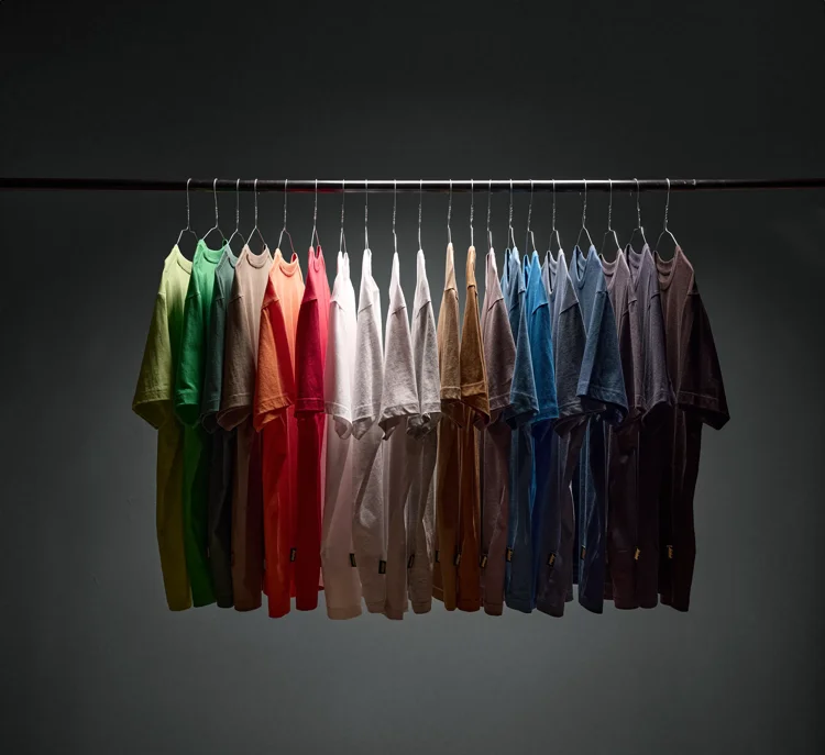 Row of colorful t-shirts hanging on a rack in a gradient rainbow of colors under a dark background