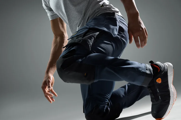Athlete mid-jump in a gray shirt and navy joggers, wearing black sneakers with orange accents.