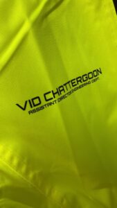 Close-up of neon yellow fabric with black text reading 'VID CHATTERGOON' and 'ASSISTANT DIRECTOR ENGINEERING DEPT.'