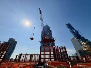 Construction crane towering over red scaffolding at a city construction site against a clear blue sky.